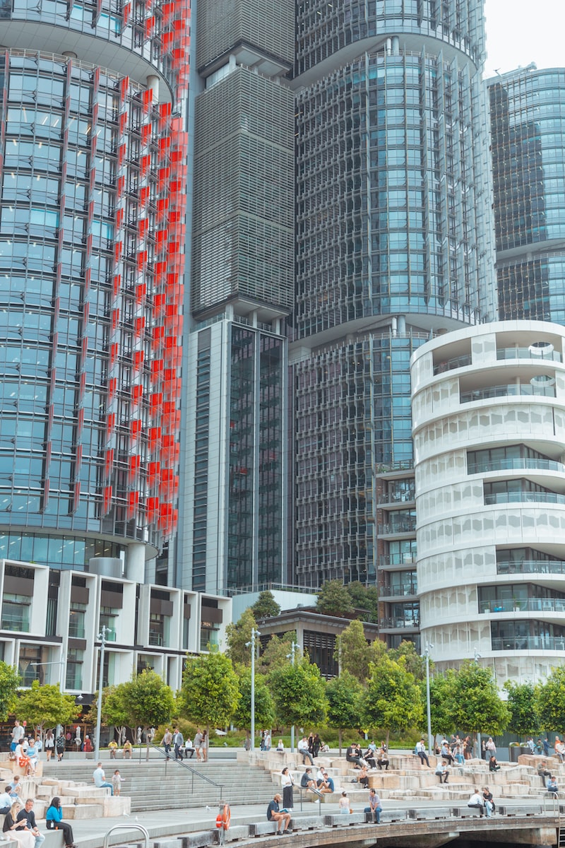 a group of people walking along a river next to tall buildings