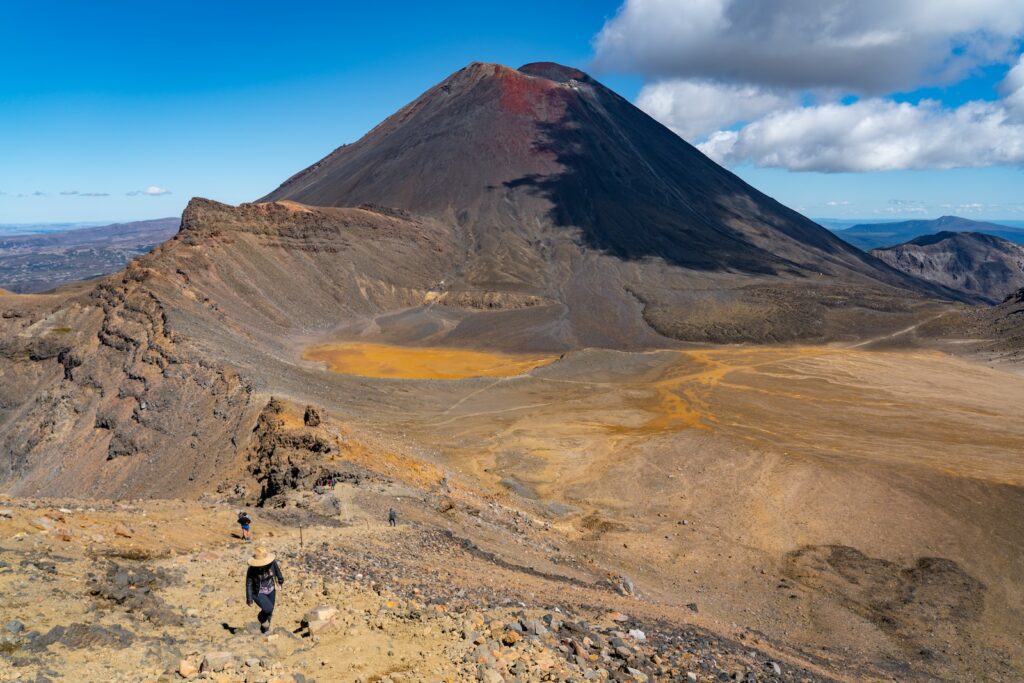 person in black jacket standing on brown sand near brown mountain under blue sky during daytime